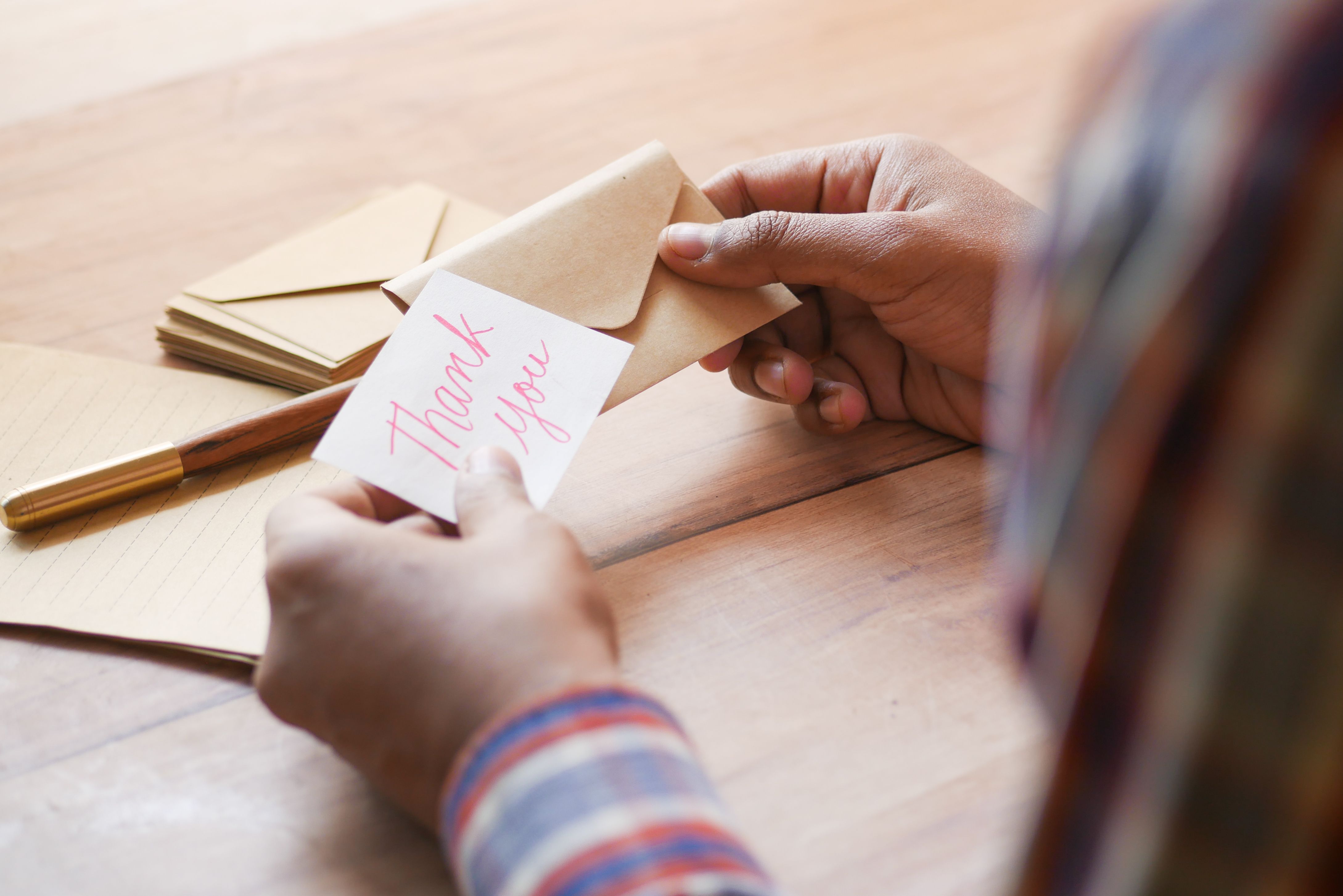 Hands holding a thank-you note in an envelope on a table